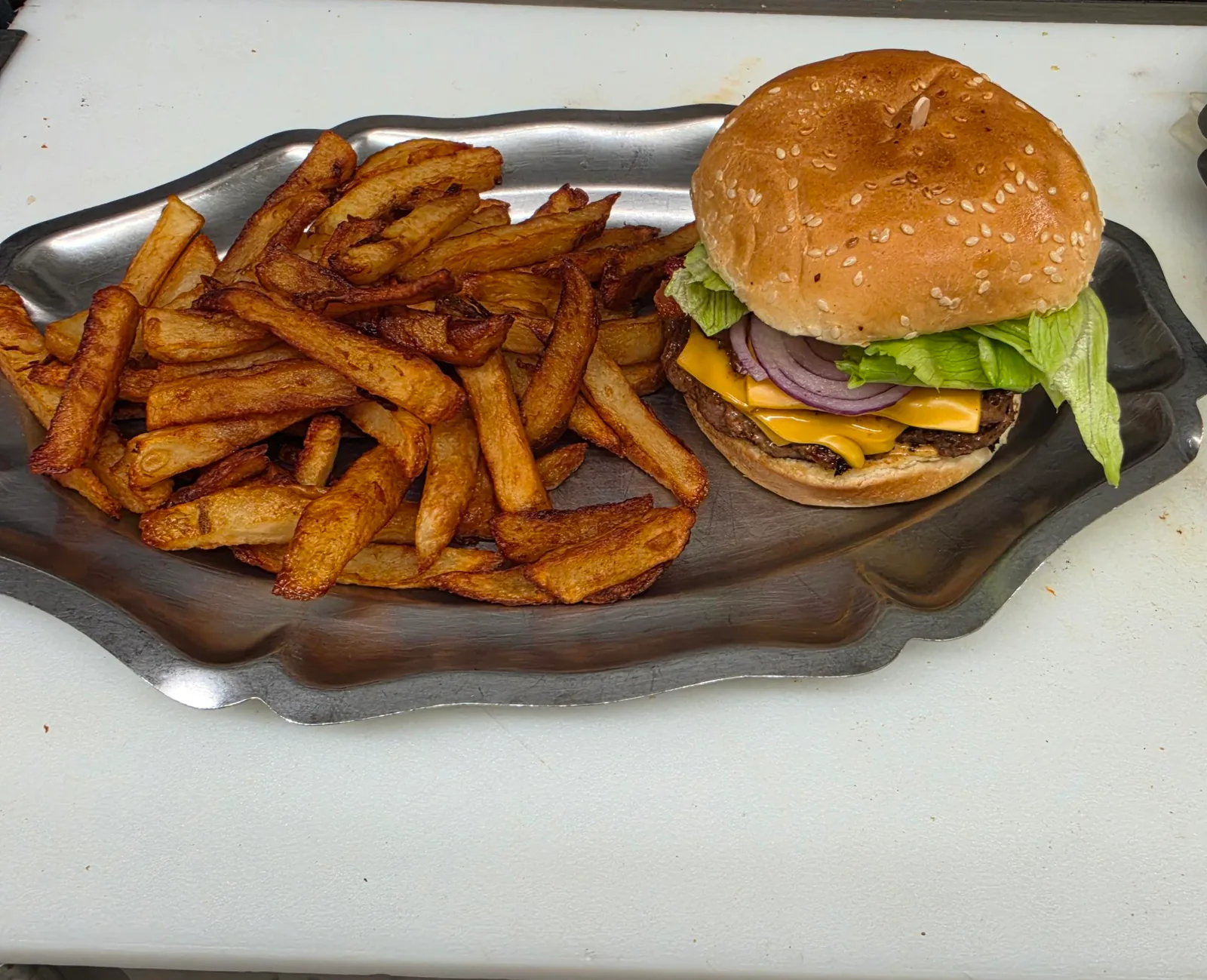 Hamburger au fromage avec oignon rouge et laitue dans un pain au sésame, servi avec des frites sur un plat en métal
