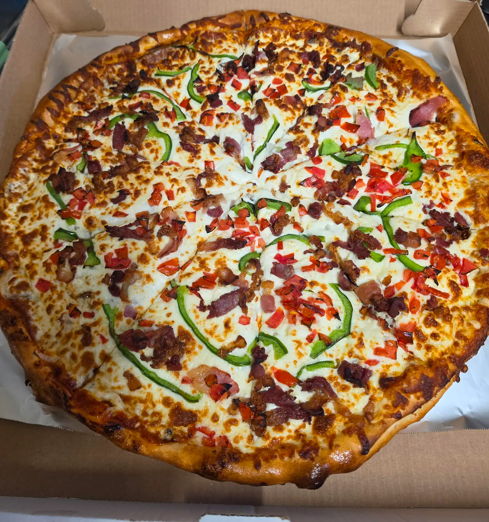 Pizza garnie de bacon, de lanières de poivron vert et de poivron rouge en dés, dans une boîte de carton ouverte