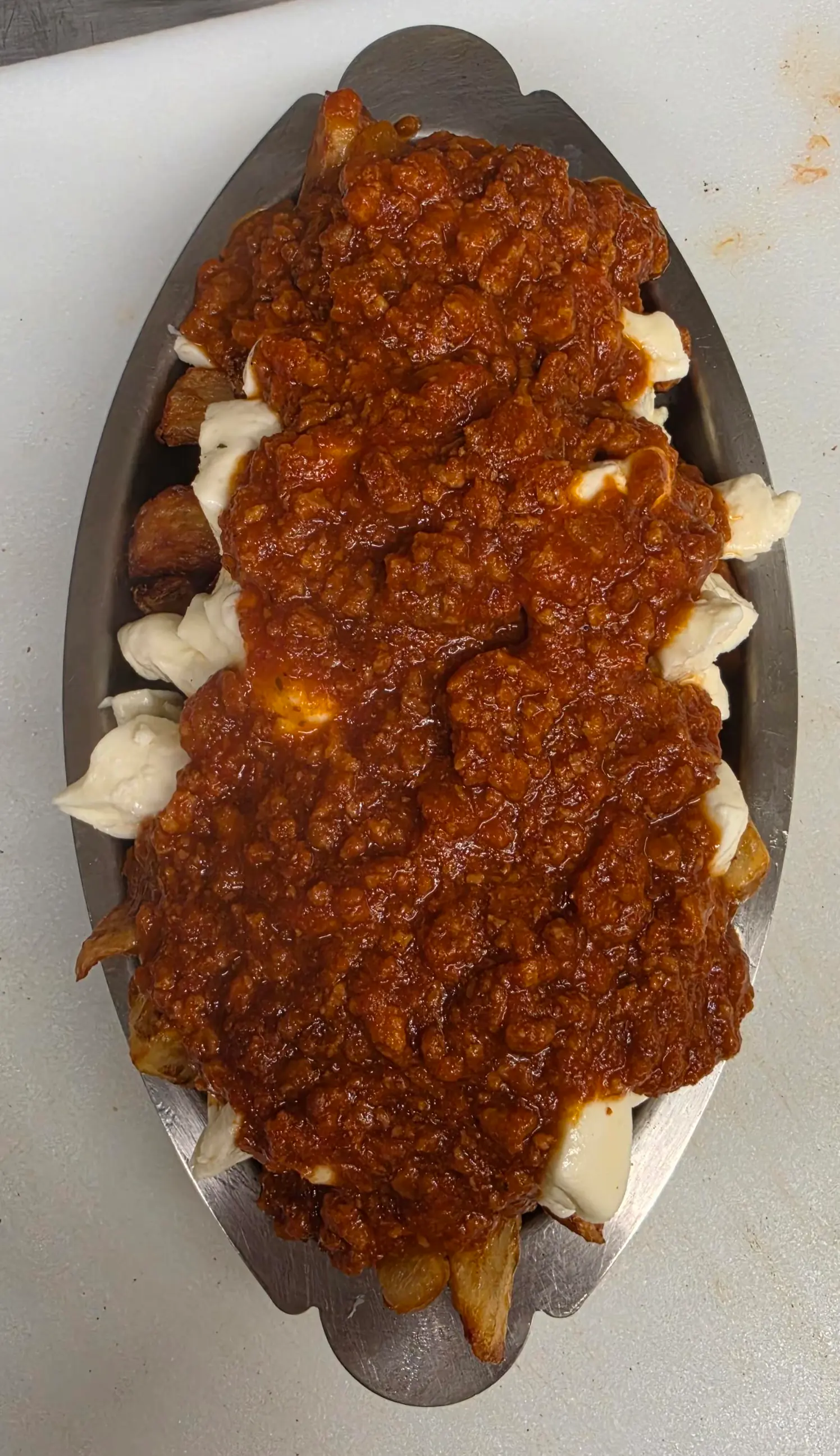 Poutine recouverte d'une sauce rouge à la viande hachée, dans un plat ovale en inox
