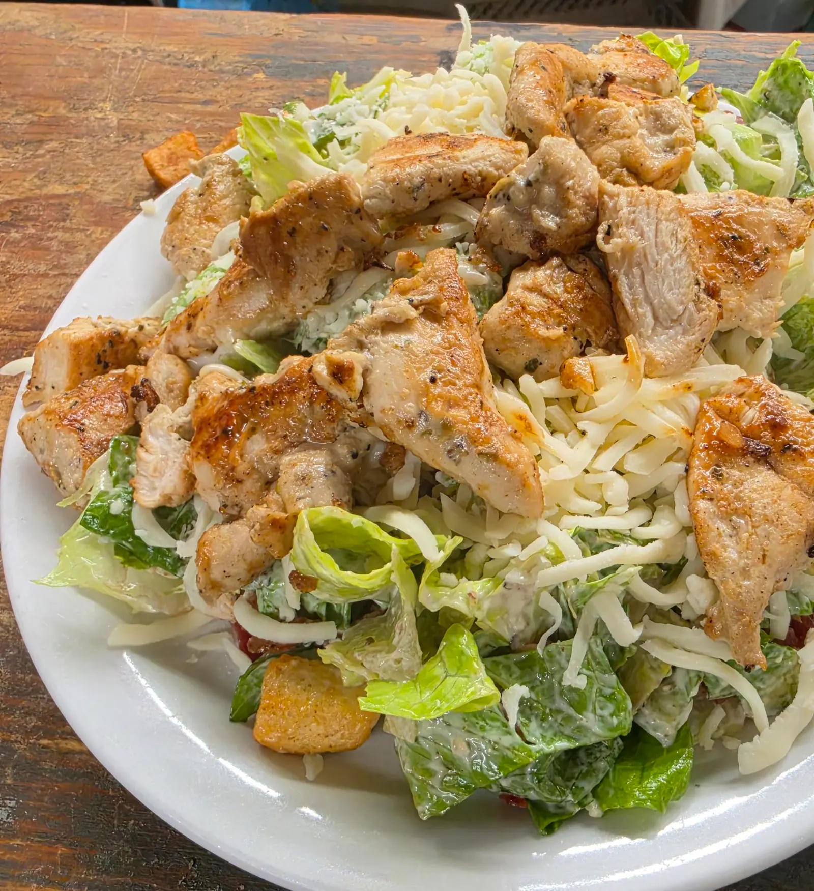 Salade de laitue romaine garnie de morceaux de poulet grillé, de fromage râpé et de croûtons, dans une assiette blanche
