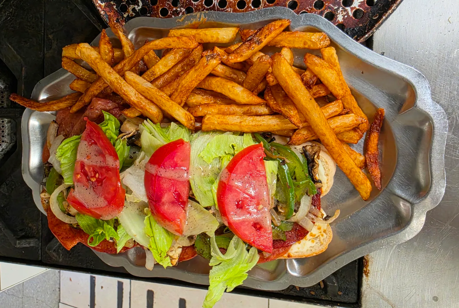 Sandwich ouvert dans un pain allongé, garni de charcuterie, de champignons, de poivron vert, de laitue et de tomate, avec des frites